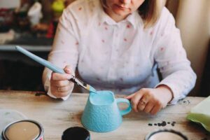 Woman painting with oil paint on ceramic mug